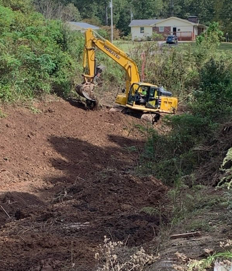 Construction equipment clearing a path through trees, stumps, and debris